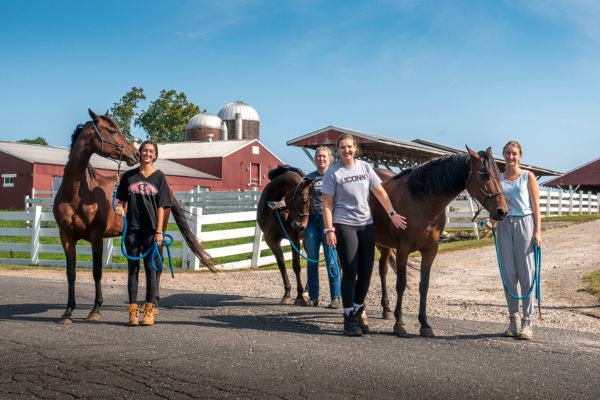 Students posing for photo with horses.