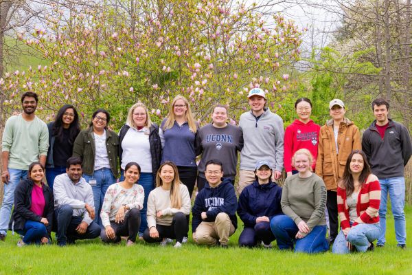 A group of students gathered together in front of a tree with pink flowers in bloom on a spring day