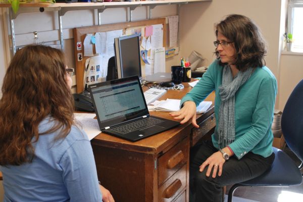 Faculty member sitting across from student inside of office and assisting them with a computer