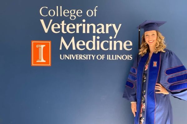 Student in cap and gown posing next to a sign reading University of Illinois College of Veterinary Medicine