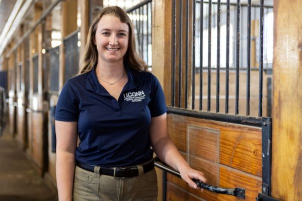 Student standing next to a a series of wooden horse stalls with metal bars