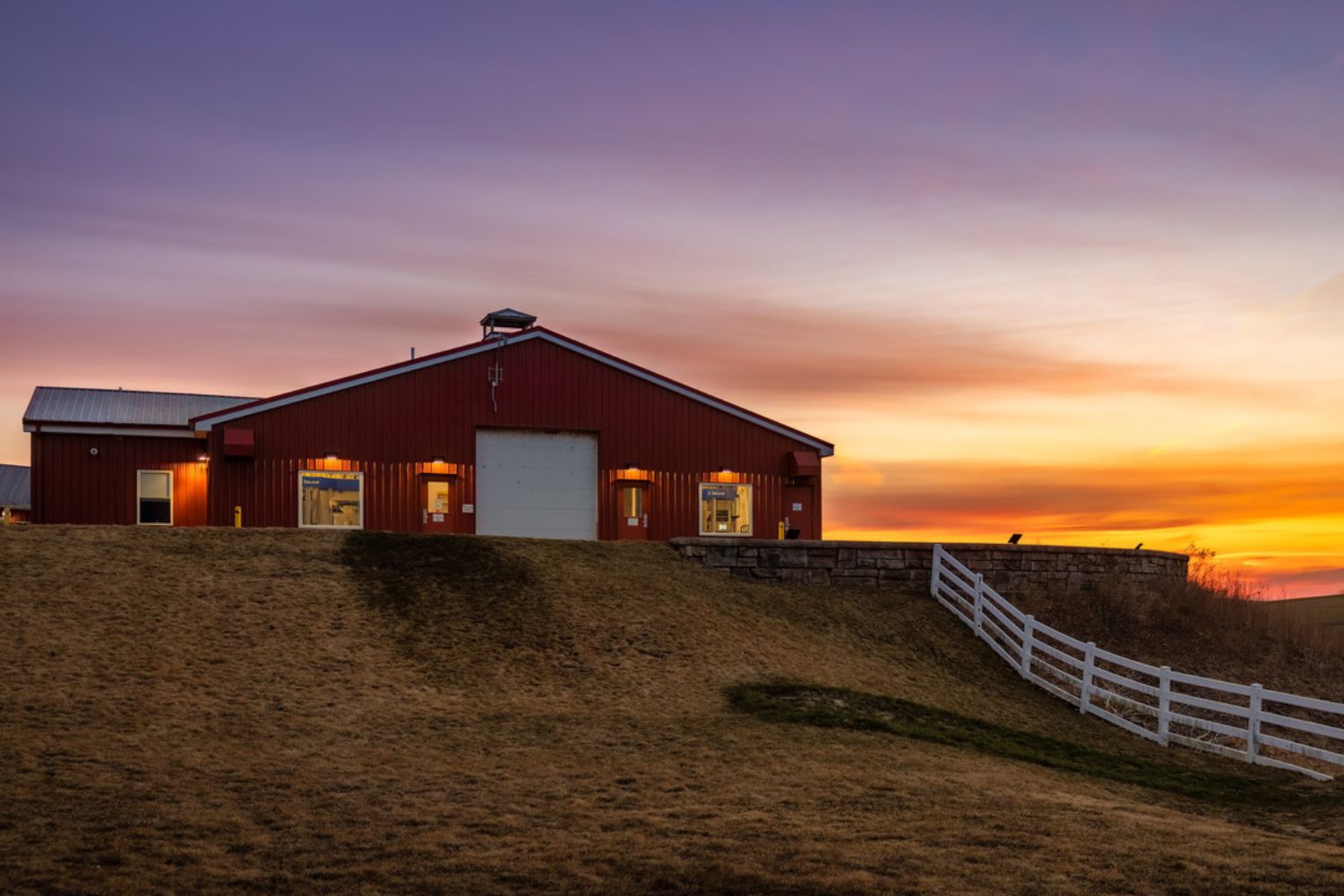 A red barn sitting on top of a hill at sunset.